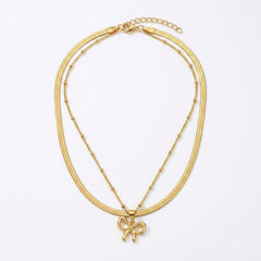 A gold double-strand necklace featuring a textured snake chain and a delicate beaded chain with a small bow pendant, displayed on a clean white background.